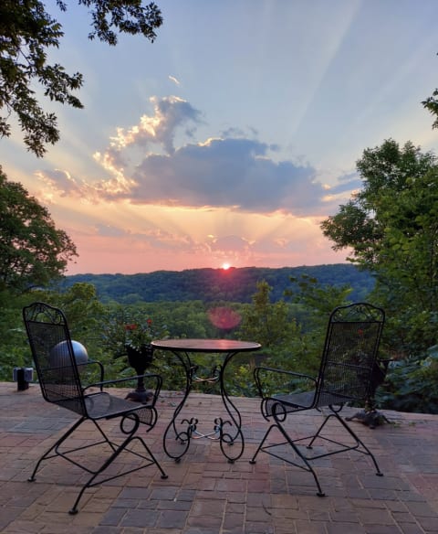 A sunset view from a patio showcasing chairs and a table, with rolling hills and colorful skies in the background.