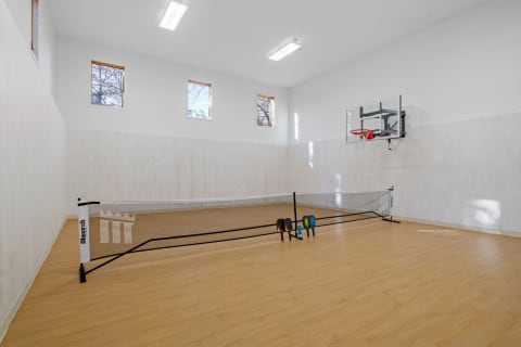 Indoor sports gym with a basketball hoop and badminton net on a wooden floor.