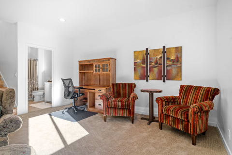 Living room featuring striped chairs, an ergonomic desk, and a bathroom doorway.
