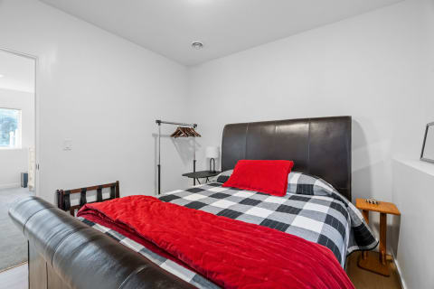 A modern bedroom featuring a leather headboard bed with checkered bedding and red accents.