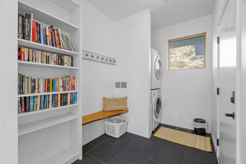 A modern laundry room with bookshelves, a bench, washing machines, and a window.