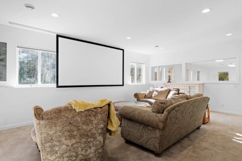 A warm living room featuring a large projection screen, comfortable sofas, and natural light.