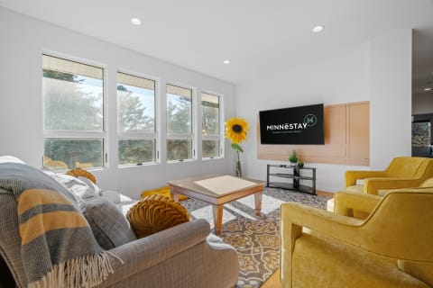Bright living room featuring a gray couch, yellow armchairs, and a flat-screen TV with branding.