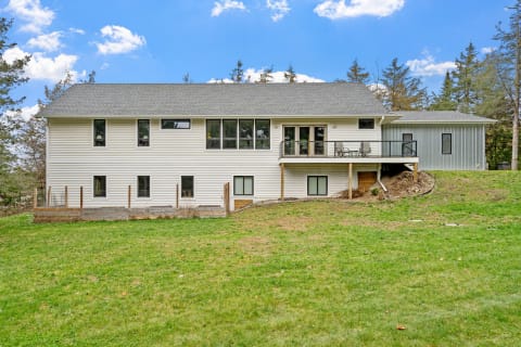 Two-story modern house with white siding and large windows, complemented by a green lawn and outdoor seating.