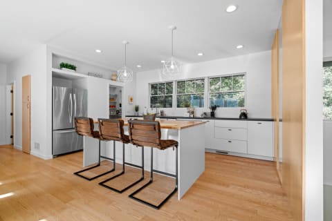Modern kitchen featuring white cabinets, a wooden island, and leather bar stools.