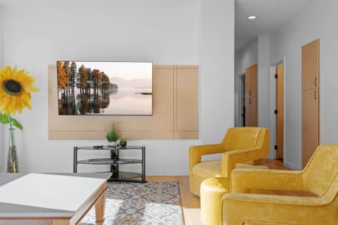 Cozy modern living room with yellow armchairs and a television displaying autumn scenery.