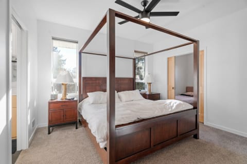 A cozy bedroom featuring a four-poster bed, bedside lamp, and natural light from large windows.