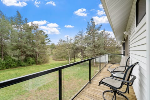 Balcony with chairs overlooking green trees and blue sky.