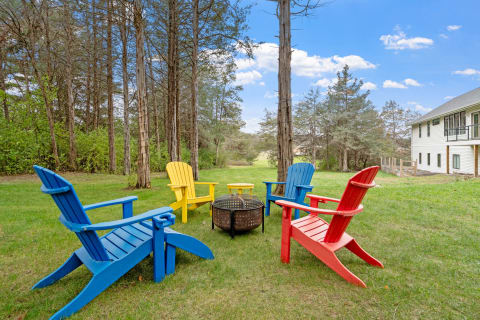 Adirondack chairs in blue, yellow, and red around a fire pit in a grassy yard.
