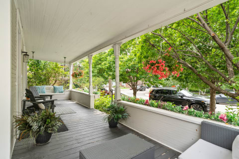 Porch area featuring wooden seating and lush plants outside a house.