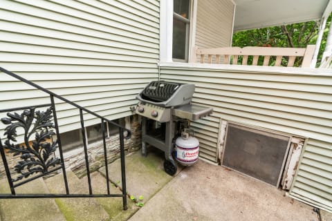 Compact outdoor grill beside a house with decorative stair railing.