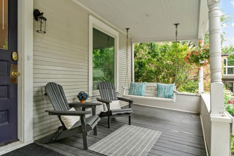 Charming porch with two chairs, a swing, and flowering plants in a vibrant setting.
