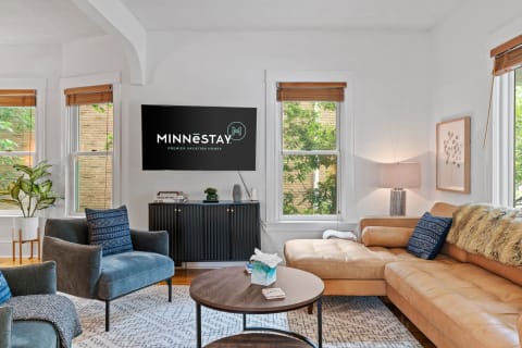 Cozy living room with a sectional sofa, decorative pillows, and a TV displaying the MINNēSTAY logo.