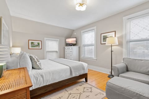 Interior of a cozy bedroom with a bed, sofa, and dresser under soft lighting.