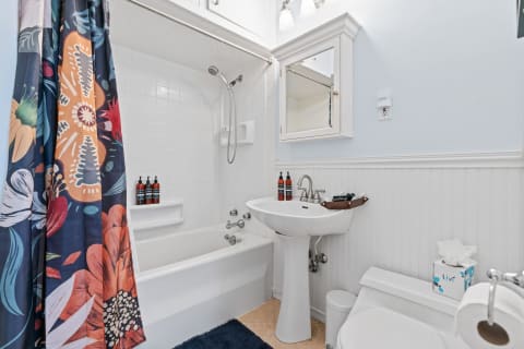 A bright bathroom with a floral shower curtain, pedestal sink, and modern decor.