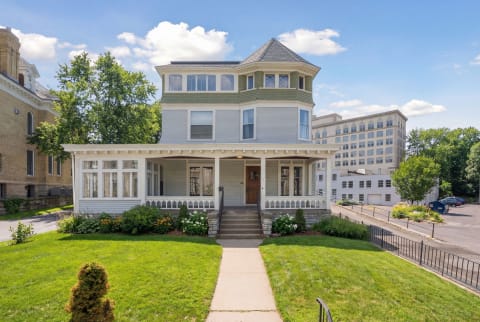 Victorian house with turret and wraparound porch in an urban environment.