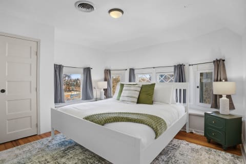 Bright corner bedroom with a white bed, natural light, and green accents.
