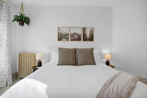 A cozy bedroom featuring a neatly made bed with patterned pillows, framed art on the wall, and warm bedside lighting.
