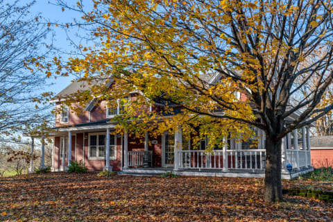 A two-story red house with autumn foliage and a porch.