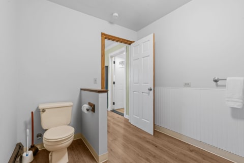 Interior view of a clean bathroom with a beige toilet, toilet paper holder, and wooden floors.