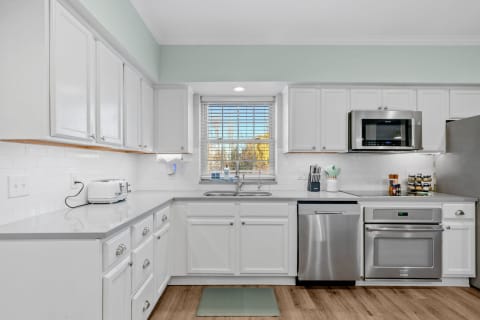A bright kitchen with white cabinets, gray countertops, and stainless steel appliances.