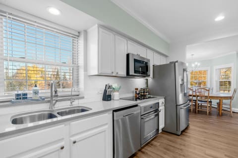 A modern kitchen featuring a double sink, stainless steel appliances, and a dining area with wooden chairs.