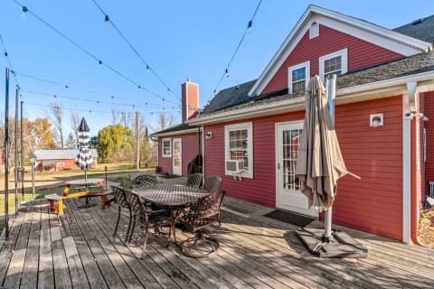 Outdoor deck with wooden flooring, a round table, chairs, and a red house in the background.