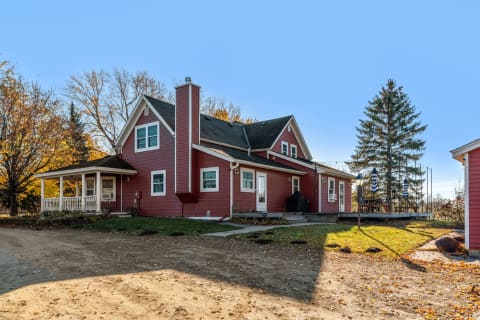 Charming red house with a porch and autumn foliage in a rural setting.