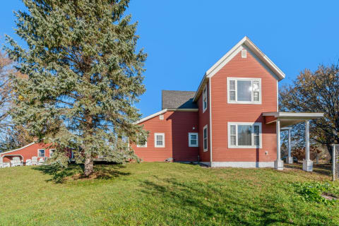 Two-story red house with a green lawn and trees on a clear day.