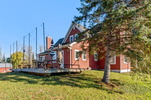 Red house with a wooden deck and patio furniture, surrounded by greenery and clear blue sky.