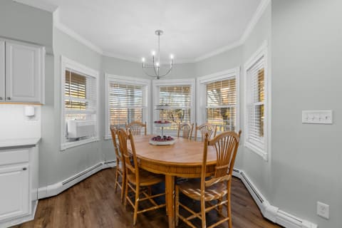 A cozy dining room featuring an oval wooden table surrounded by chairs and bay windows with blinds.