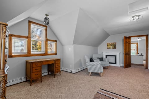 A cozy attic room featuring a desk, striped armchairs, and an elegant fireplace.