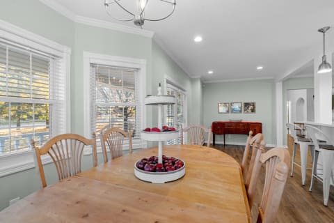 A dining room featuring a wooden table with a tiered stand of red apples and large windows with green walls.