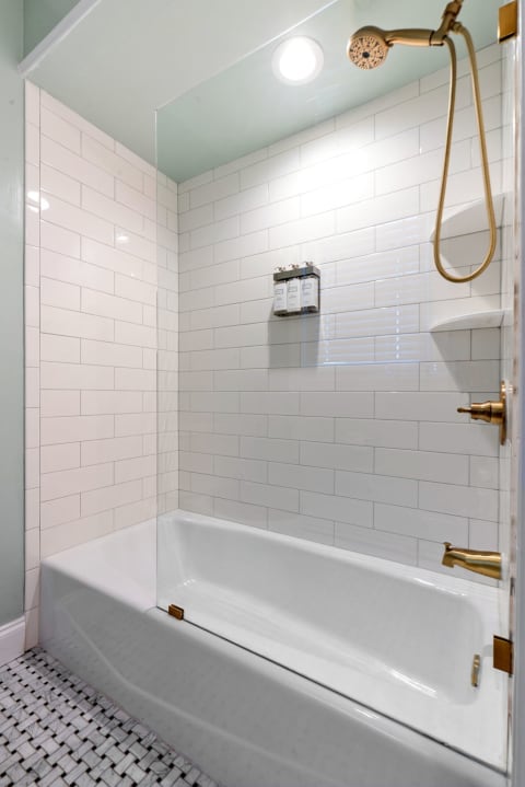 Contemporary shower area featuring white subway tiles, brass fixtures, and mosaic flooring.
