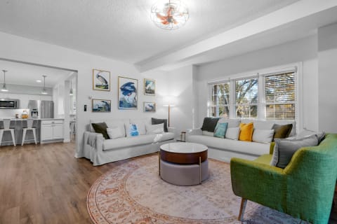 Cozy living room featuring white sofas, colorful pillows, bird illustrations on the wall, and a circular coffee table.