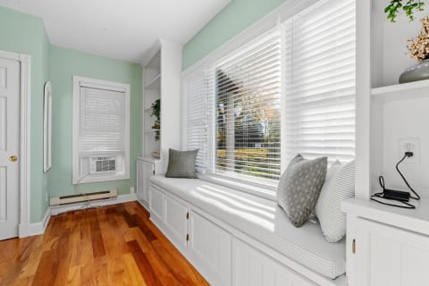 Bright sunroom with a window seat, decorative pillows, and wooden flooring.