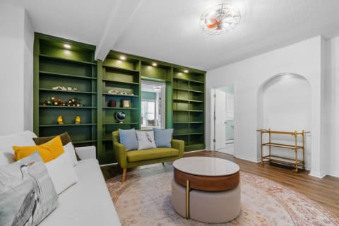 Cozy modern living room with a white sofa, colorful pillows, and a green bookshelf.