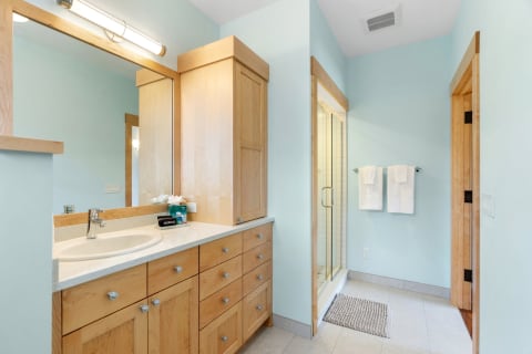 Modern bathroom with light blue walls, wooden cabinets, and a glass shower enclosure.
