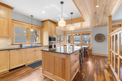 A modern kitchen featuring light wood cabinetry, dark granite countertops, and a large island.