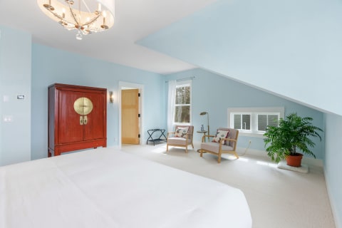 Stylish bedroom featuring blue walls, a red armoire, two armchairs, and a potted plant.