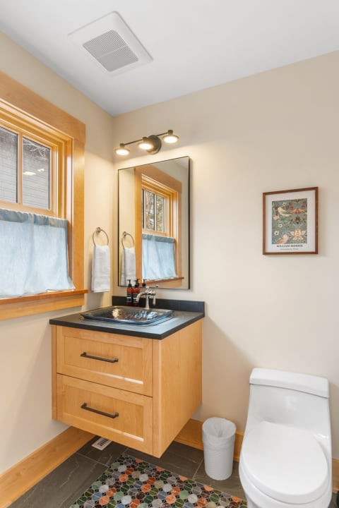 A modern bathroom interior with light-colored walls, decorative mirror, dark countertop, and a colored mosaic floor.
