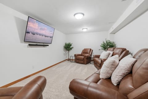 A cozy lounge area featuring leather recliners, a large TV display, and a soft carpet floor.