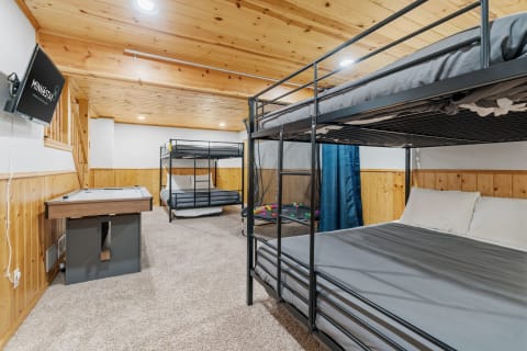 A modern basement room featuring bunk beds, a queen-size bed, and an air hockey table.