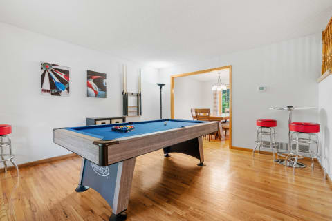 Game room featuring a blue pool table, artworks on the wall, and a dining area in the background.