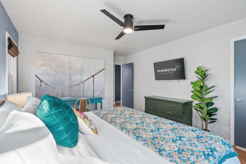 Modern bedroom with white linens, colorful throw blanket, and a calming mural of a rope bridge.