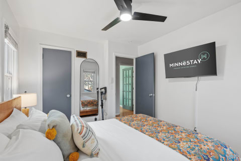 A cozy bedroom featuring a bed with colorful pillows, a flat-screen TV, and a mirror.