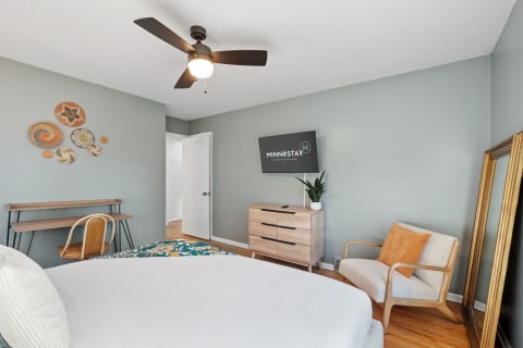 Cozy bedroom featuring a bed, desk, armchair, and minimalist decor in soft colors.