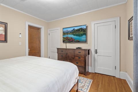 A cozy bedroom featuring a wooden dresser and a flat-screen TV with a mountain lake view.