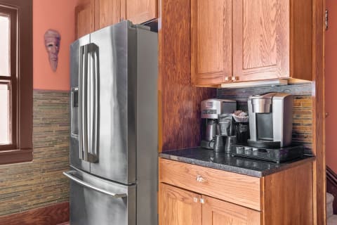A kitchen with a stainless steel fridge, wooden cabinetry, and a coffee maker on a dark countertop.
