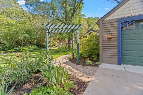 Green pergola leading into a lush garden with a winding brick path.